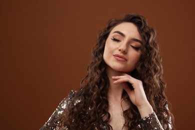 Photo of Beautiful young woman with long curly hair in sequin dress on brown background, space for text