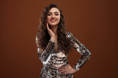 Photo of Beautiful young woman with long curly hair in sequin dress on brown background