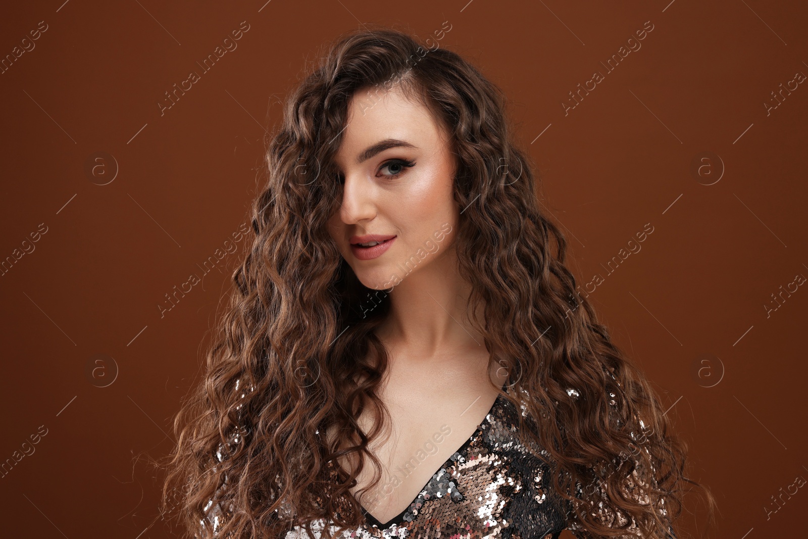 Photo of Beautiful young woman with long curly hair in sequin dress on brown background