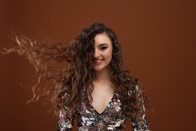 Photo of Beautiful young woman with long curly hair in sequin dress on brown background