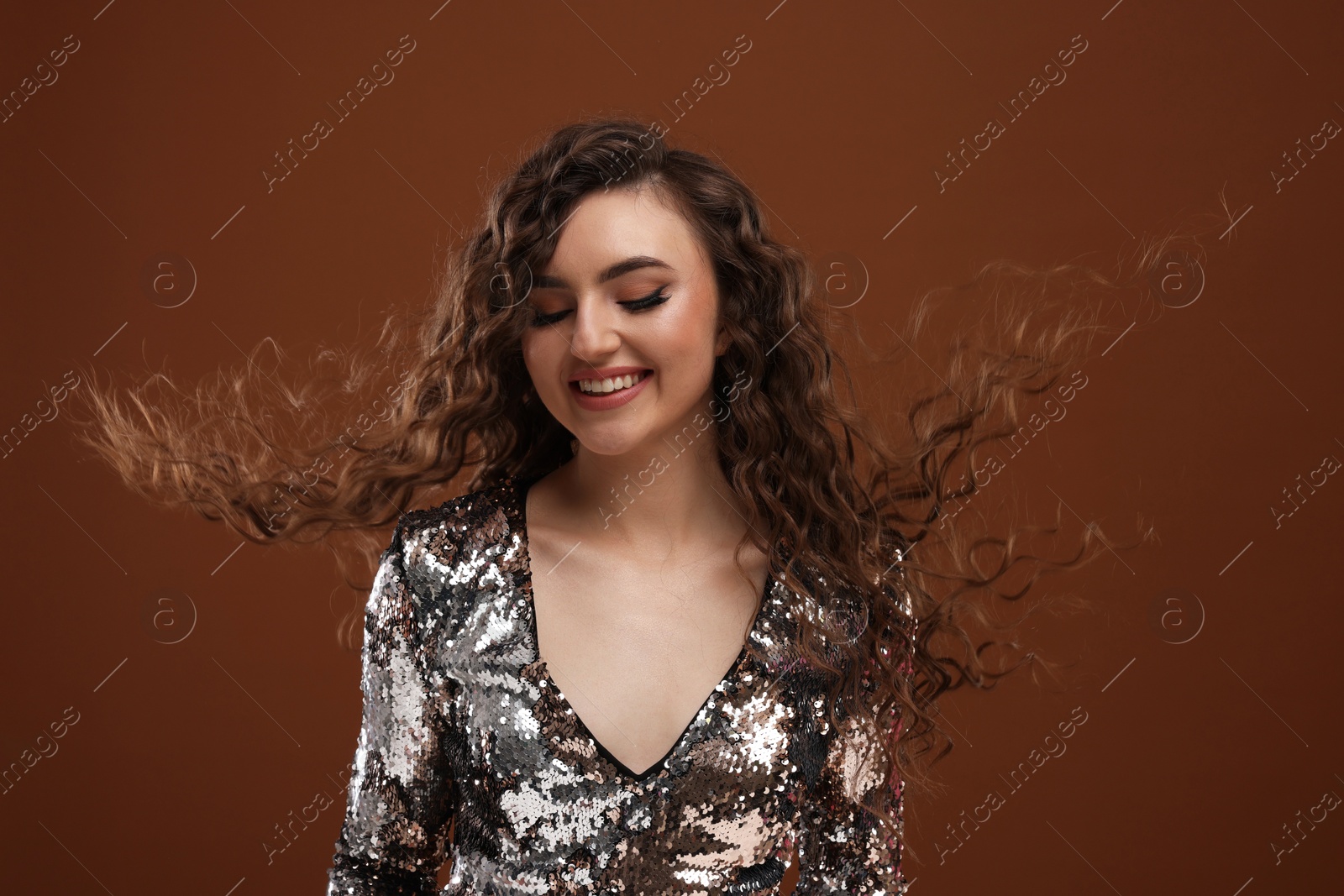 Photo of Beautiful young woman with long curly hair in sequin dress on brown background