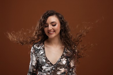 Photo of Beautiful young woman with long curly hair in sequin dress on brown background