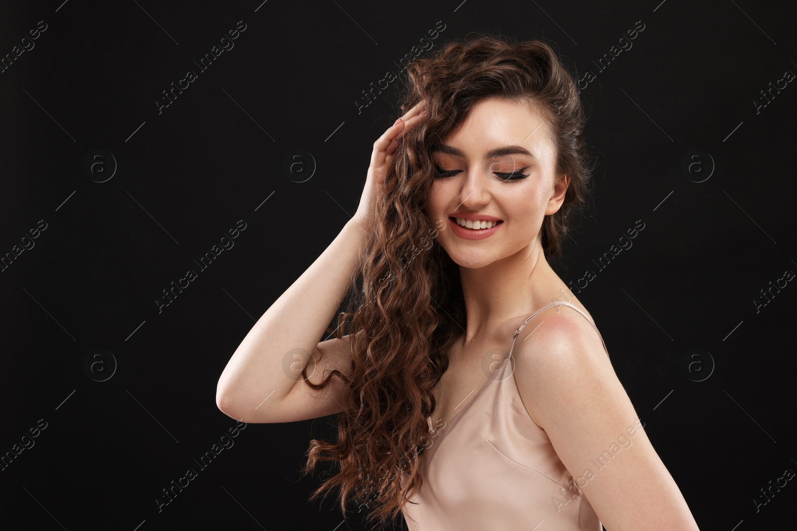 Photo of Beautiful young woman with long curly brown hair on black background, space for text