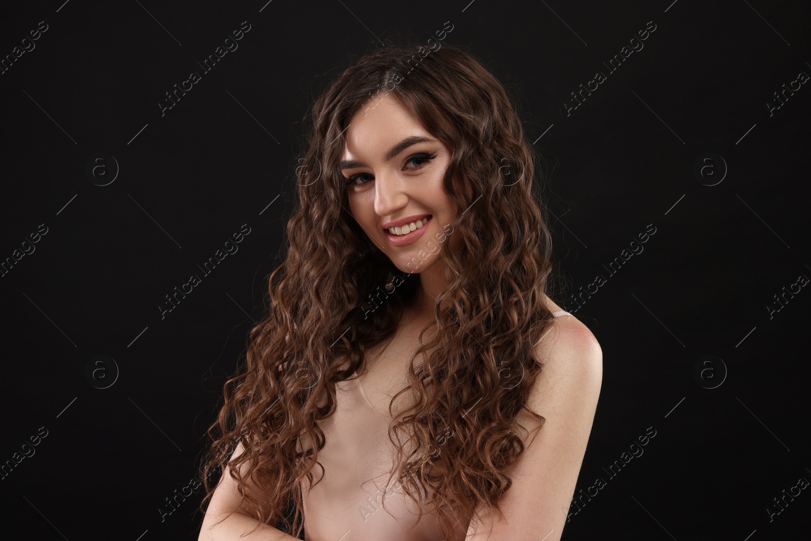 Photo of Beautiful young woman with long curly brown hair on black background