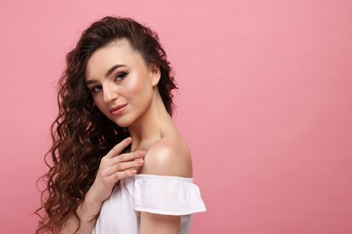 Photo of Beautiful young woman with long curly brown hair on pink background, space for text