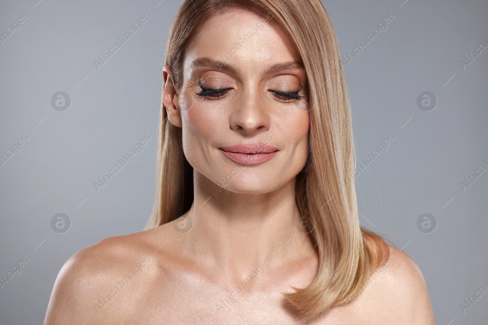 Photo of Portrait of beautiful woman with straight blonde hair and stylish makeup on grey background