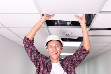 Photo of Suspended ceiling installation. Builder working with PVC tile indoors