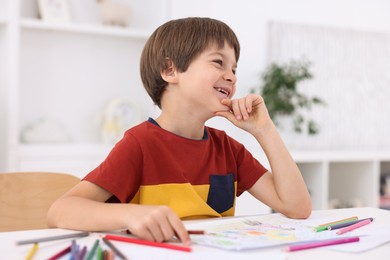 Photo of Happy boy at white table with drawing in kindergarten