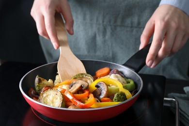 Photo of Woman frying vegetables and mushrooms in pan on stove, closeup