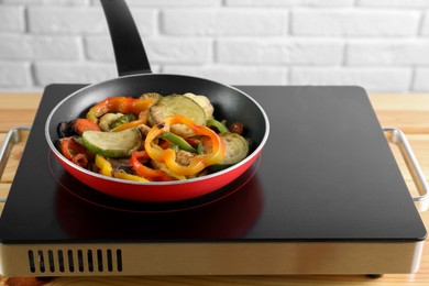 Photo of Frying pan with vegetables and stove on wooden table indoors, closeup