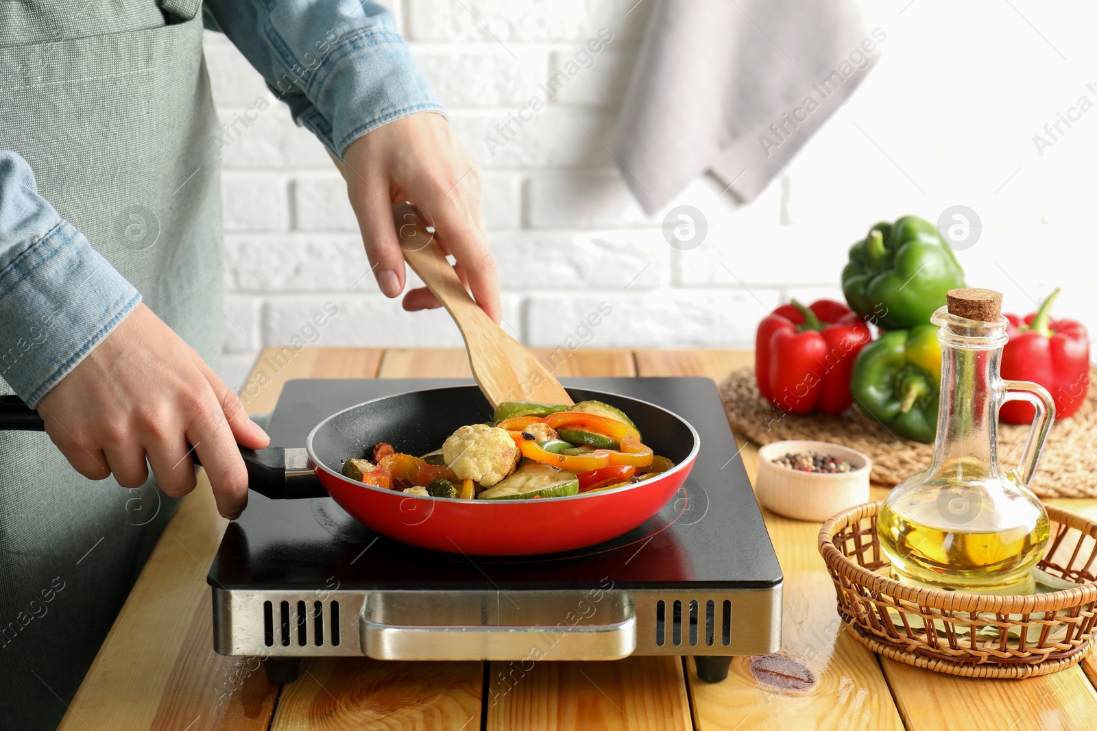 Photo of Woman frying vegetables in pan on stove at wooden table indoors, closeup