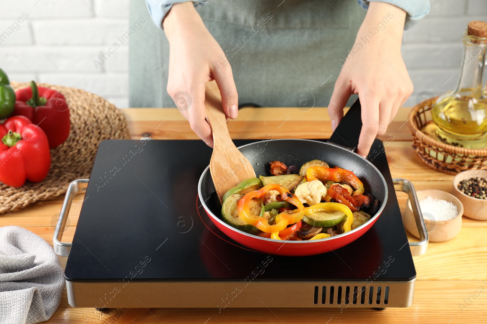 Photo of Woman frying vegetables in pan on stove at wooden table indoors, closeup