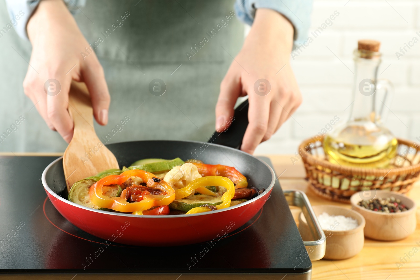 Photo of Woman frying vegetables in pan on stove at wooden table indoors, closeup