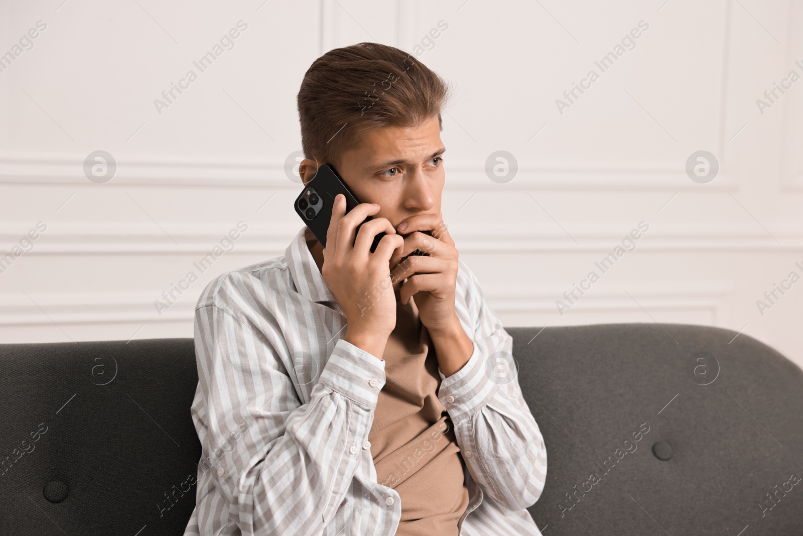 Photo of Worried man calling hotline for mental health help on sofa at home