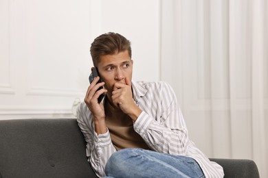 Photo of Worried man calling hotline for mental health help on sofa at home