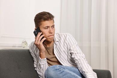 Photo of Worried man calling hotline for mental health help on sofa at home