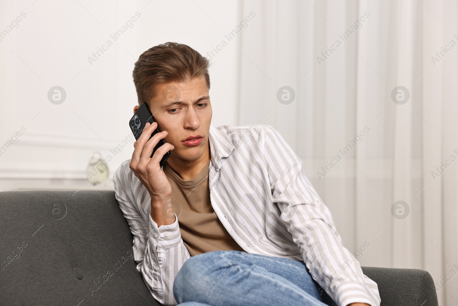 Photo of Worried man calling hotline for mental health help on sofa at home