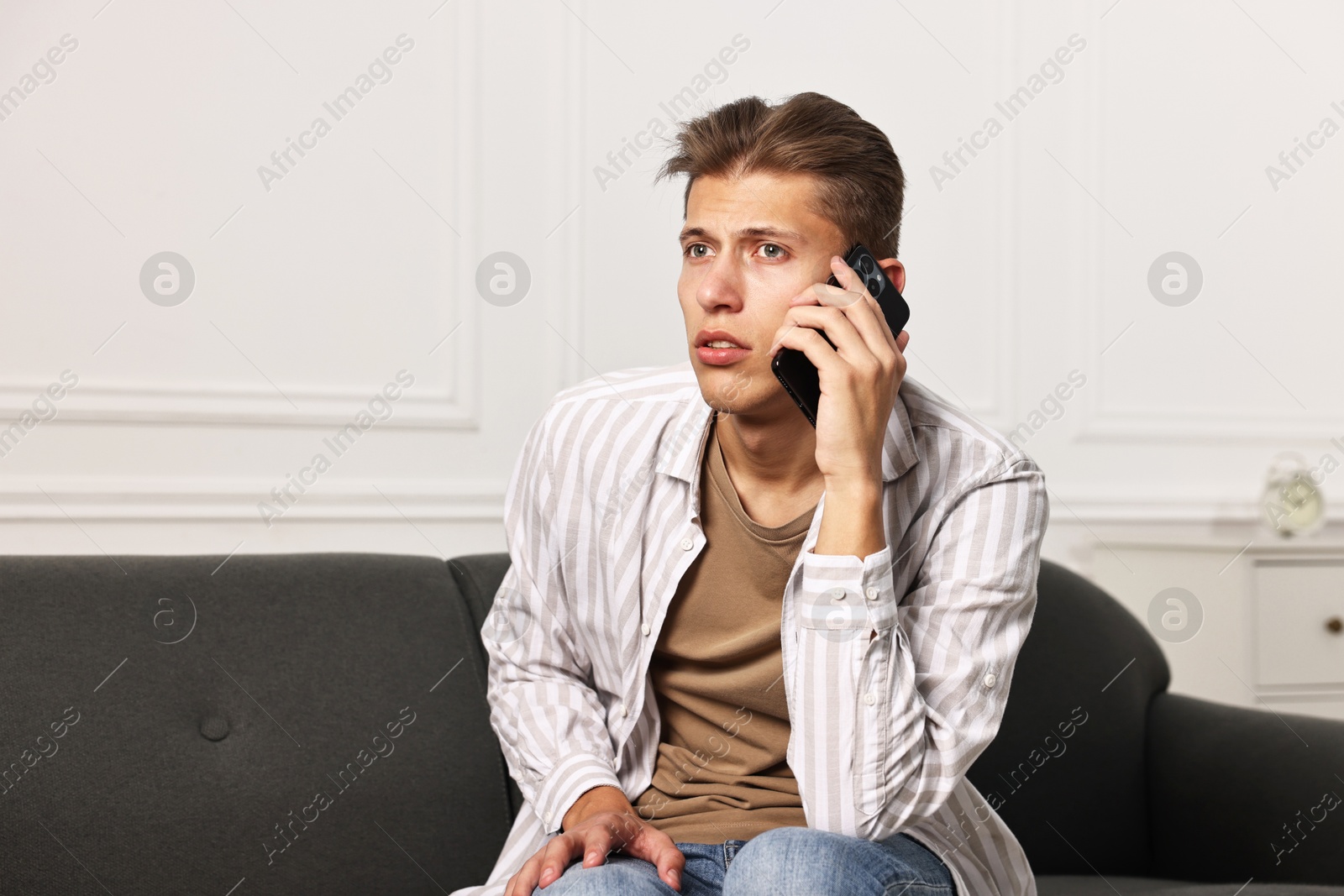 Photo of Worried man calling hotline for mental health help on sofa at home. Space for text