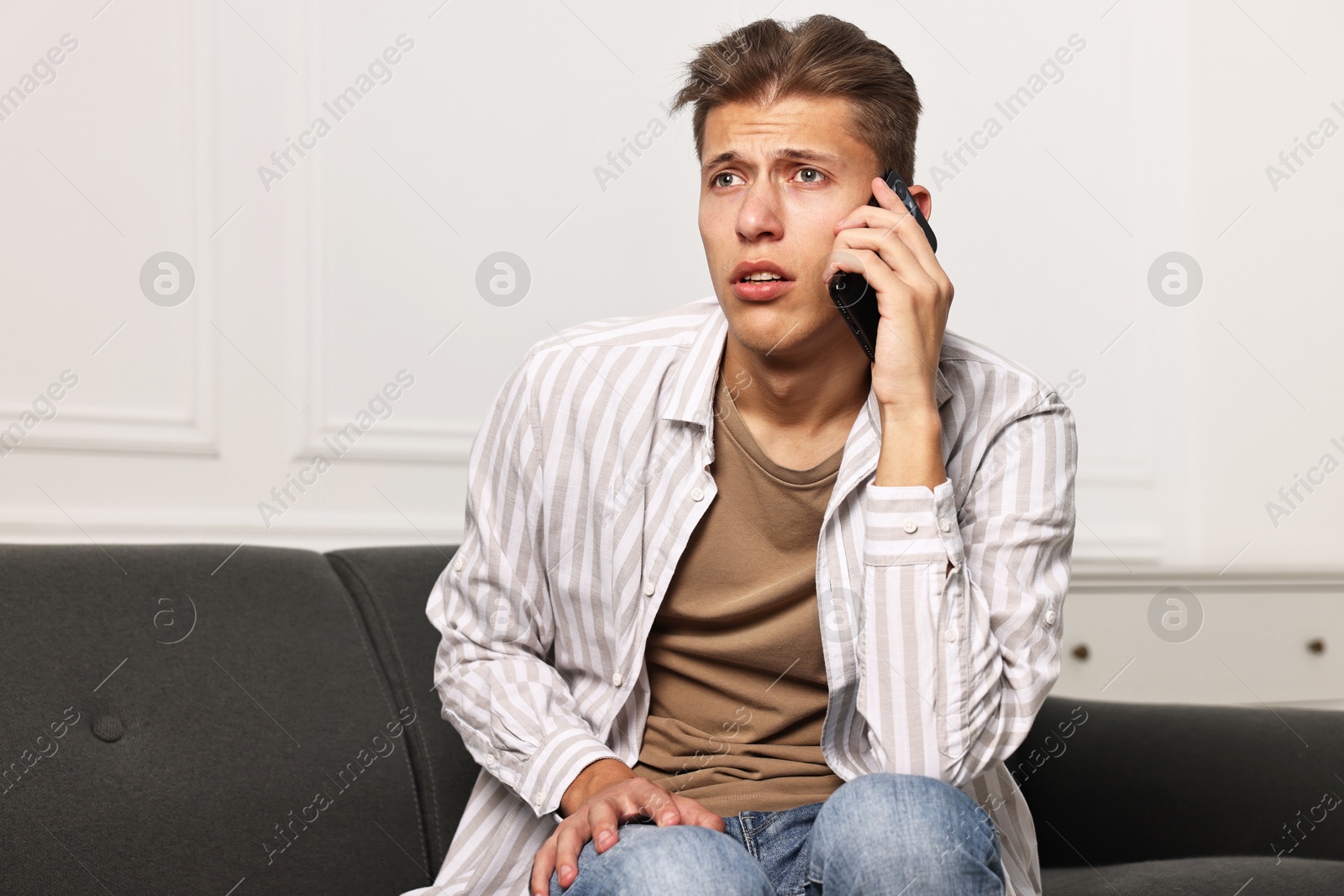 Photo of Worried man calling hotline for mental health help on sofa at home. Space for text