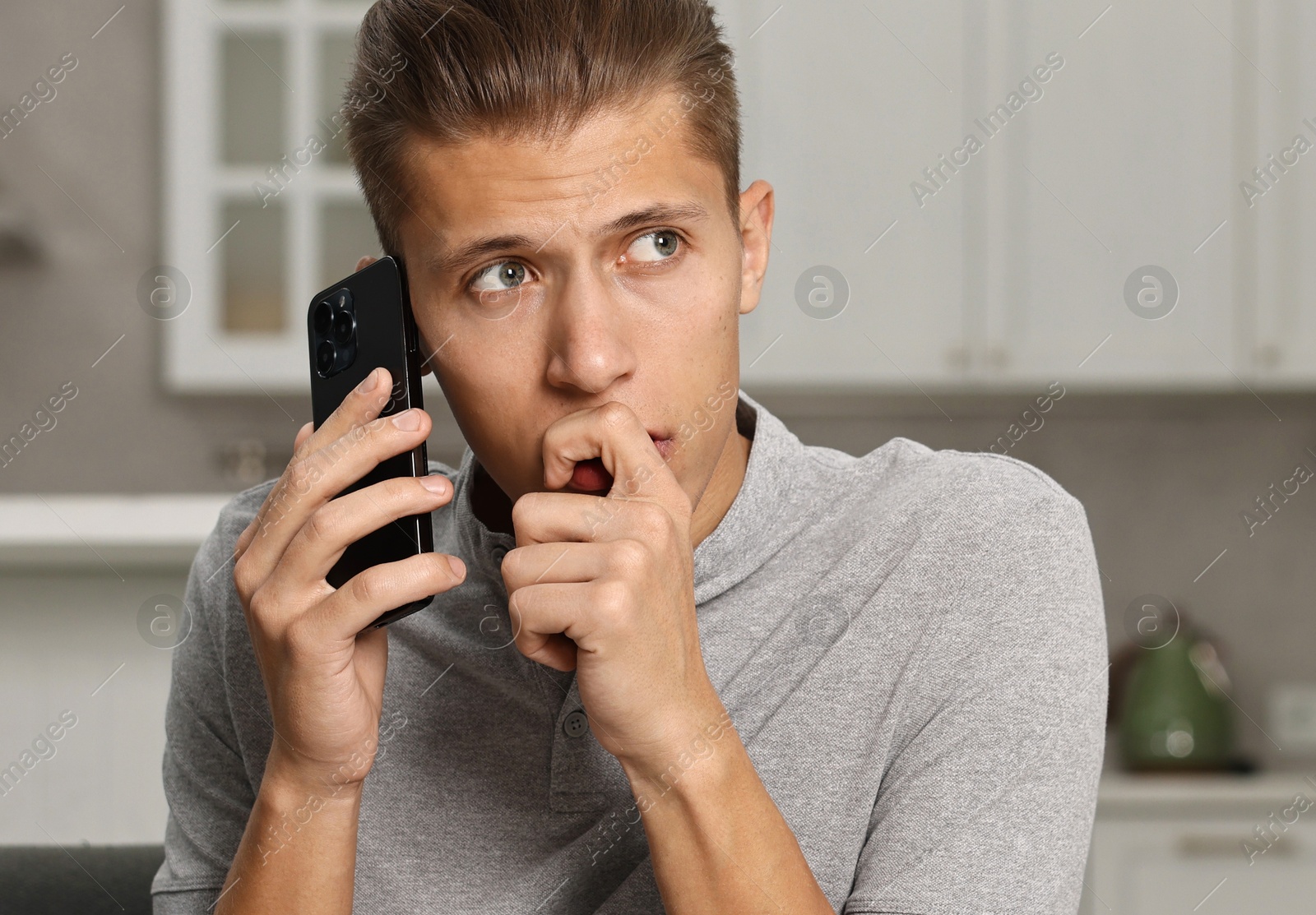 Photo of Stressed man calling hotline for mental health help on sofa in kitchen