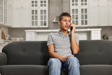 Photo of Stressed man calling hotline for mental health help on sofa in kitchen