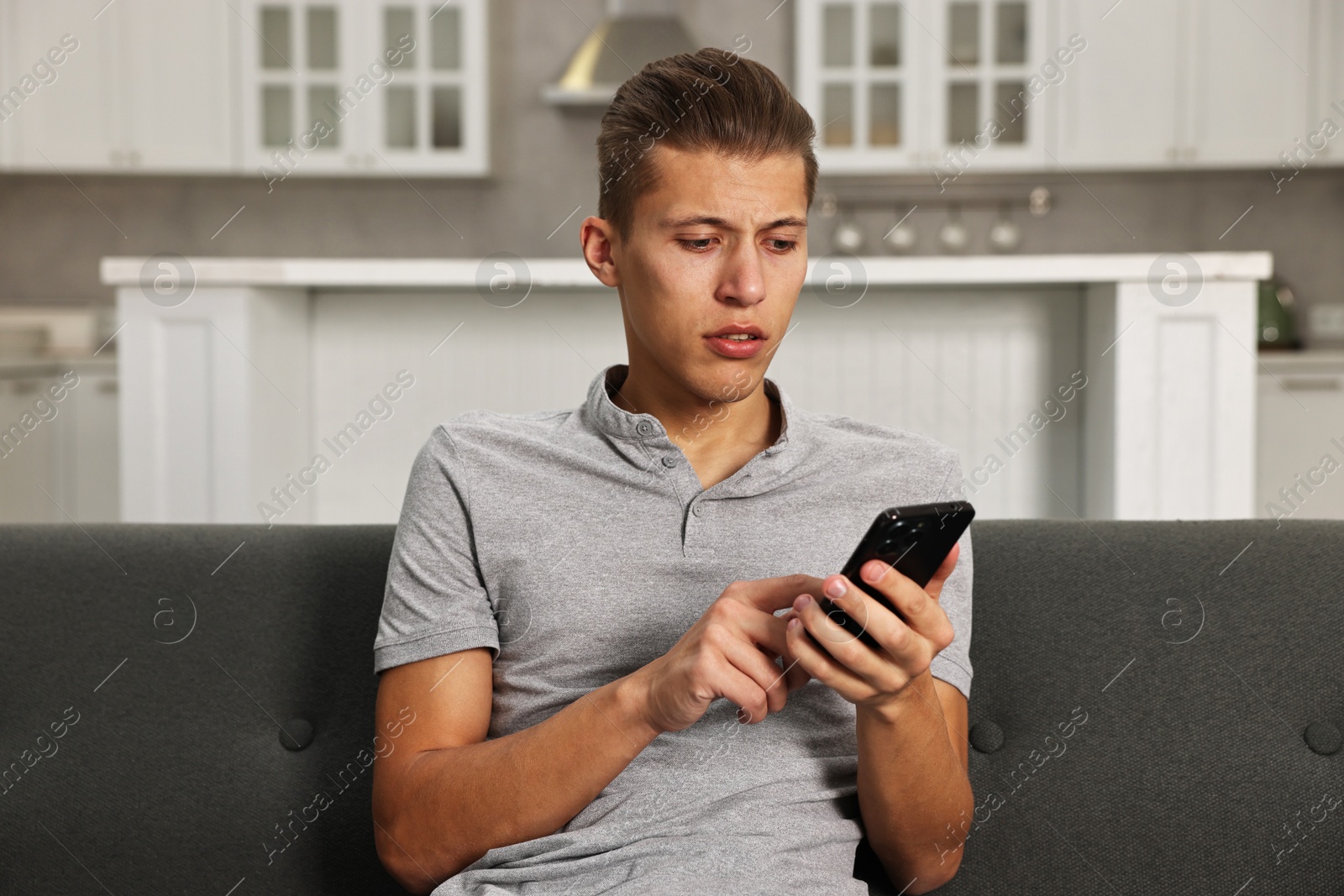 Photo of Stressed man calling hotline for mental health help on sofa in kitchen