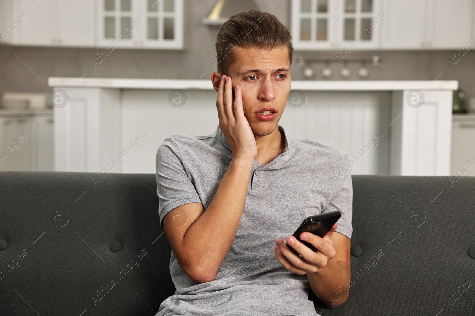 Photo of Worried man going to call hotline for mental health help on sofa in kitchen. Need for talk