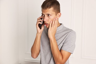 Photo of Stressed man calling hotline for mental health help indoors