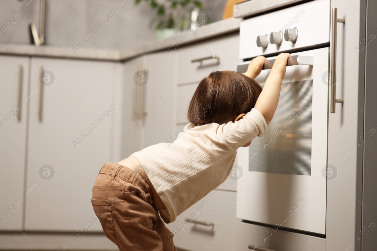 Photo of Little boy playing with oven in kitchen. Dangerous situation