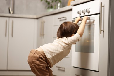 Photo of Little boy playing with oven in kitchen. Dangerous situation