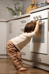 Photo of Little boy playing with oven in kitchen. Dangerous situation