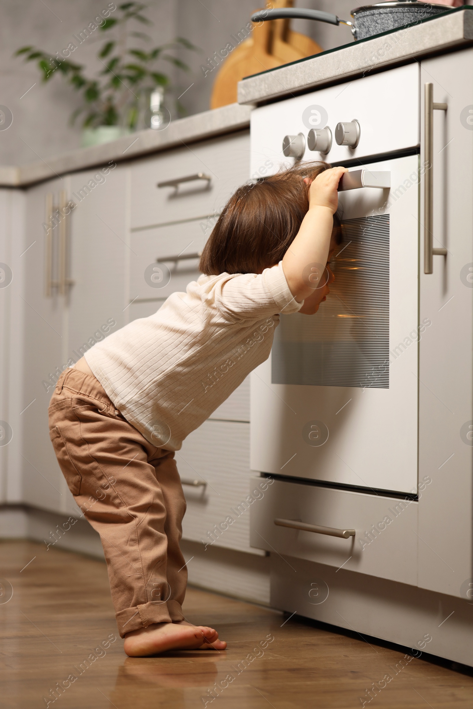 Photo of Little boy playing with oven in kitchen. Dangerous situation