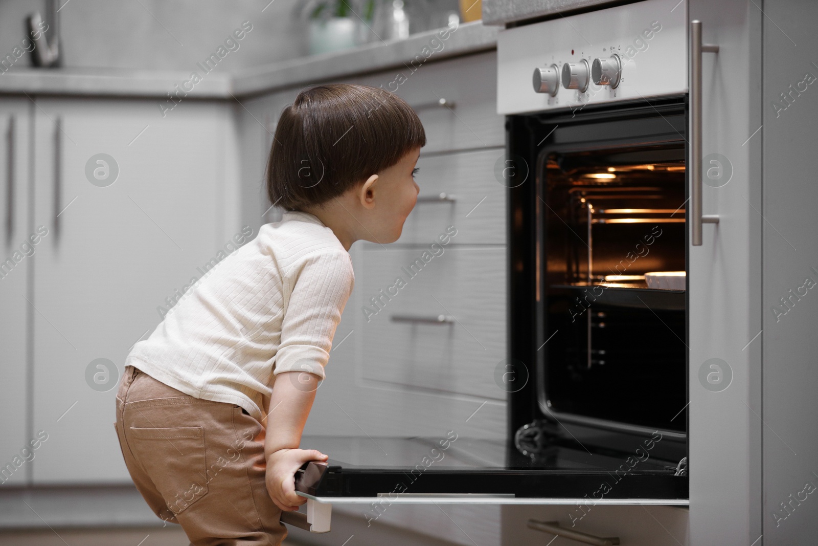 Photo of Little boy playing with oven in kitchen. Dangerous situation