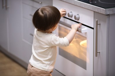 Photo of Little boy playing with oven in kitchen. Dangerous situation