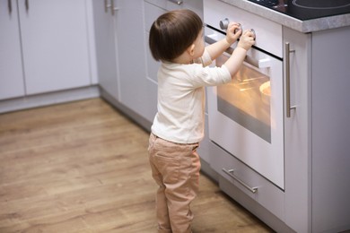 Photo of Little boy playing with oven in kitchen. Dangerous situation