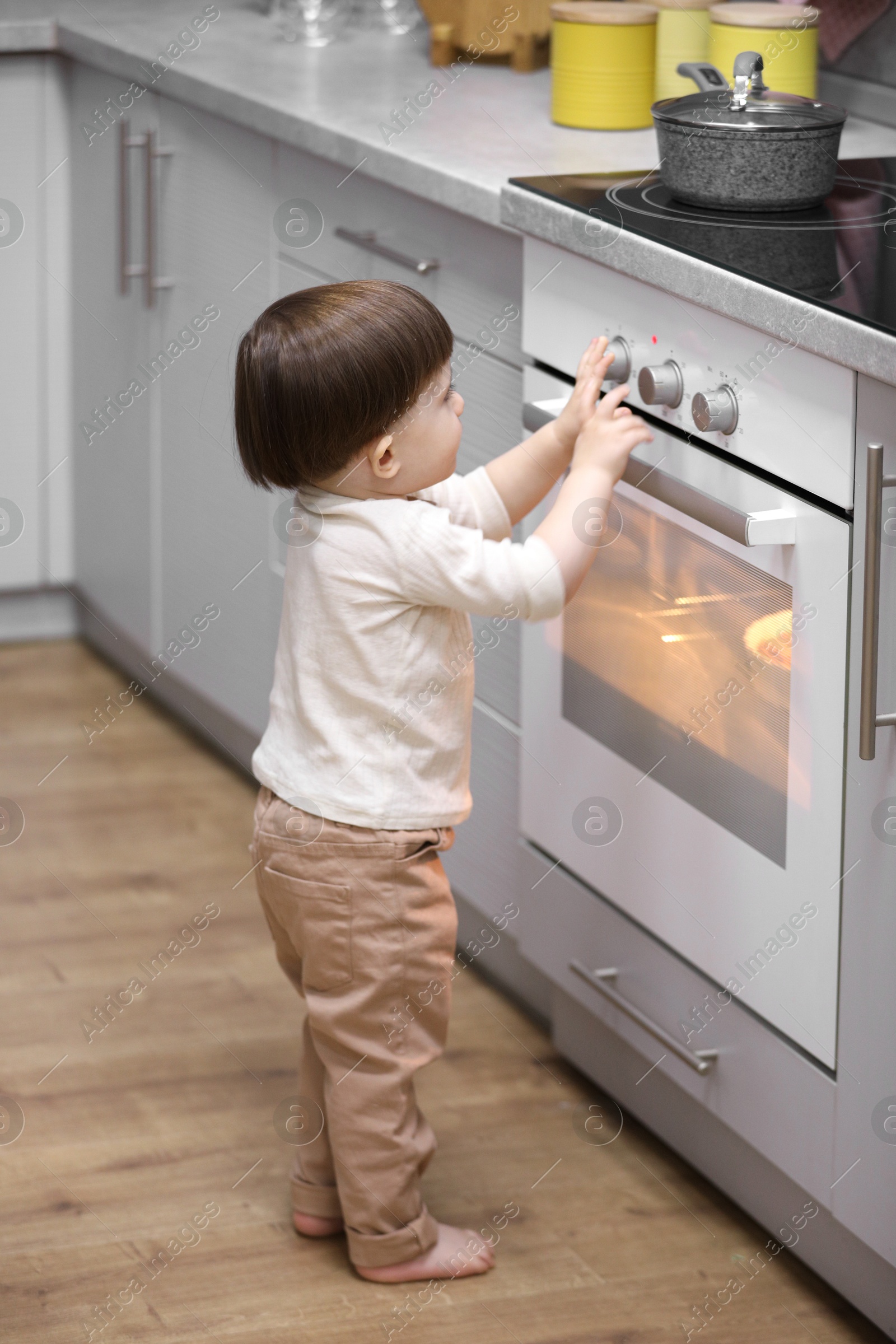 Photo of Little boy playing with oven in kitchen. Dangerous situation