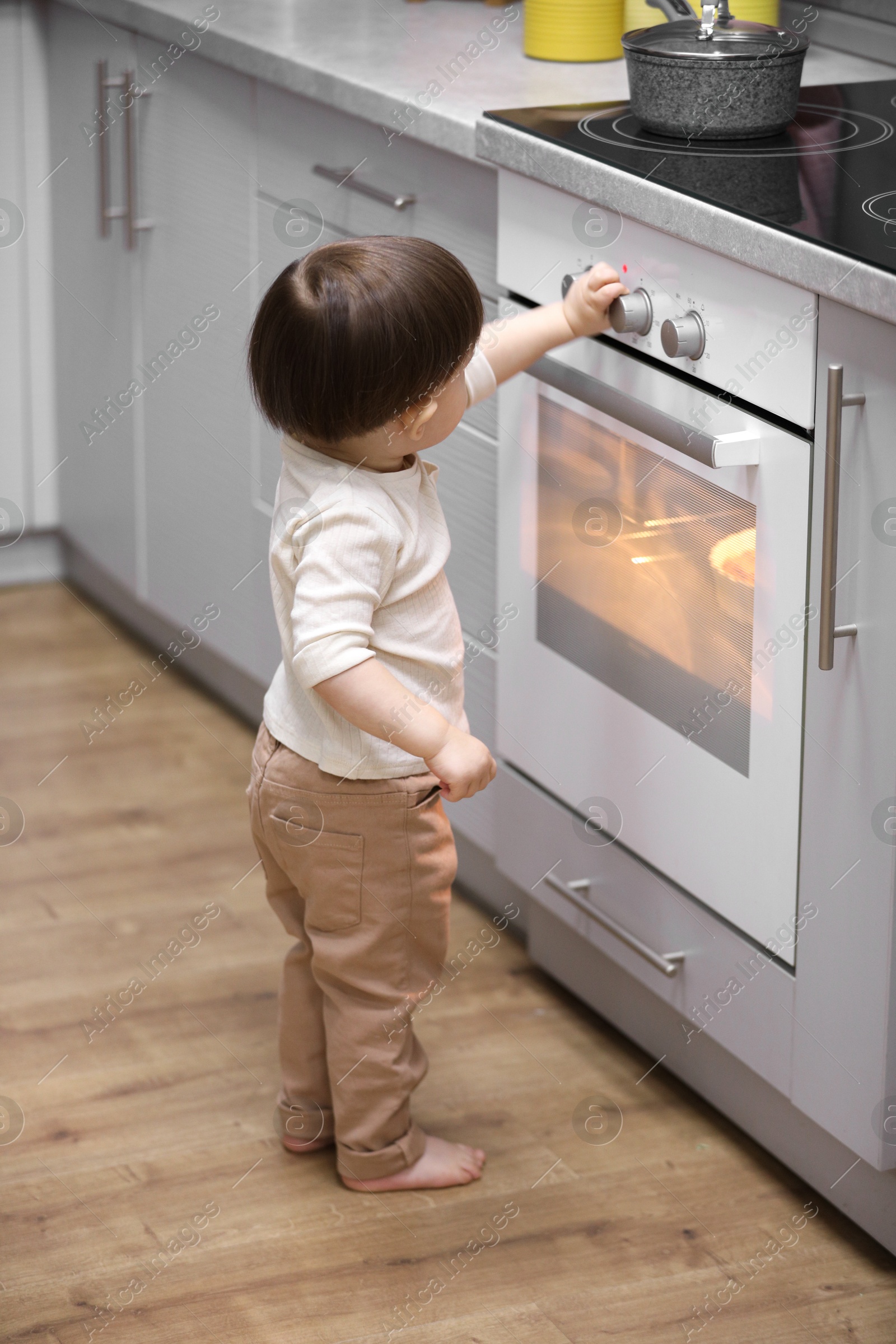 Photo of Little boy playing with oven in kitchen. Dangerous situation