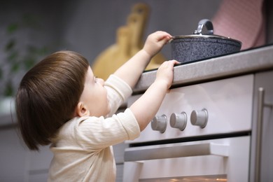 Photo of Little boy playing with pot on stove in kitchen. Dangerous situation