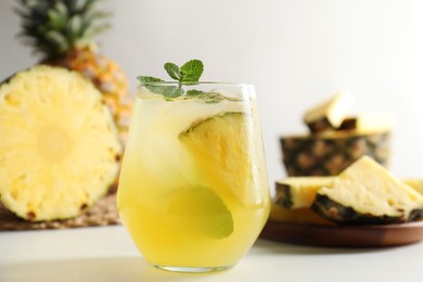 Photo of Tasty pineapple cocktail with mint in glass on light table, closeup