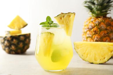 Photo of Tasty pineapple cocktail with mint in glass on light table, closeup