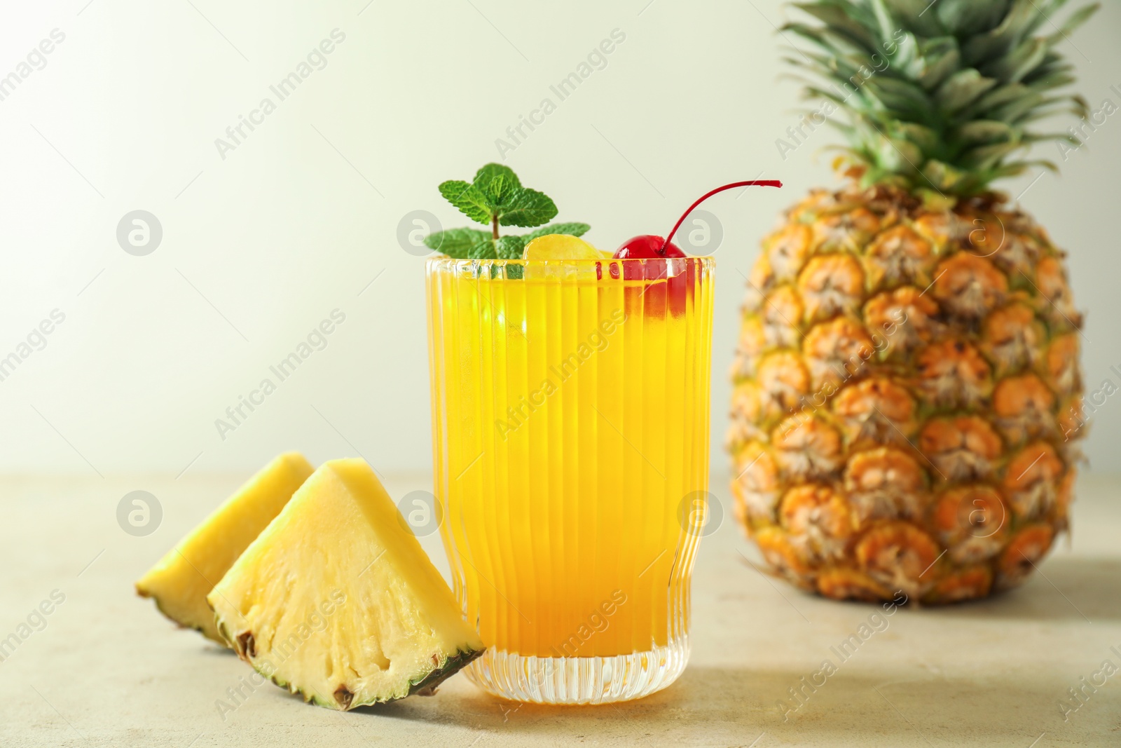 Photo of Tasty pineapple cocktail with mint and cherry in glass served on light table