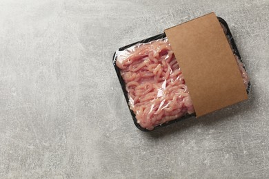 Photo of Plastic pack with fresh minced meat on grey textured table, top view