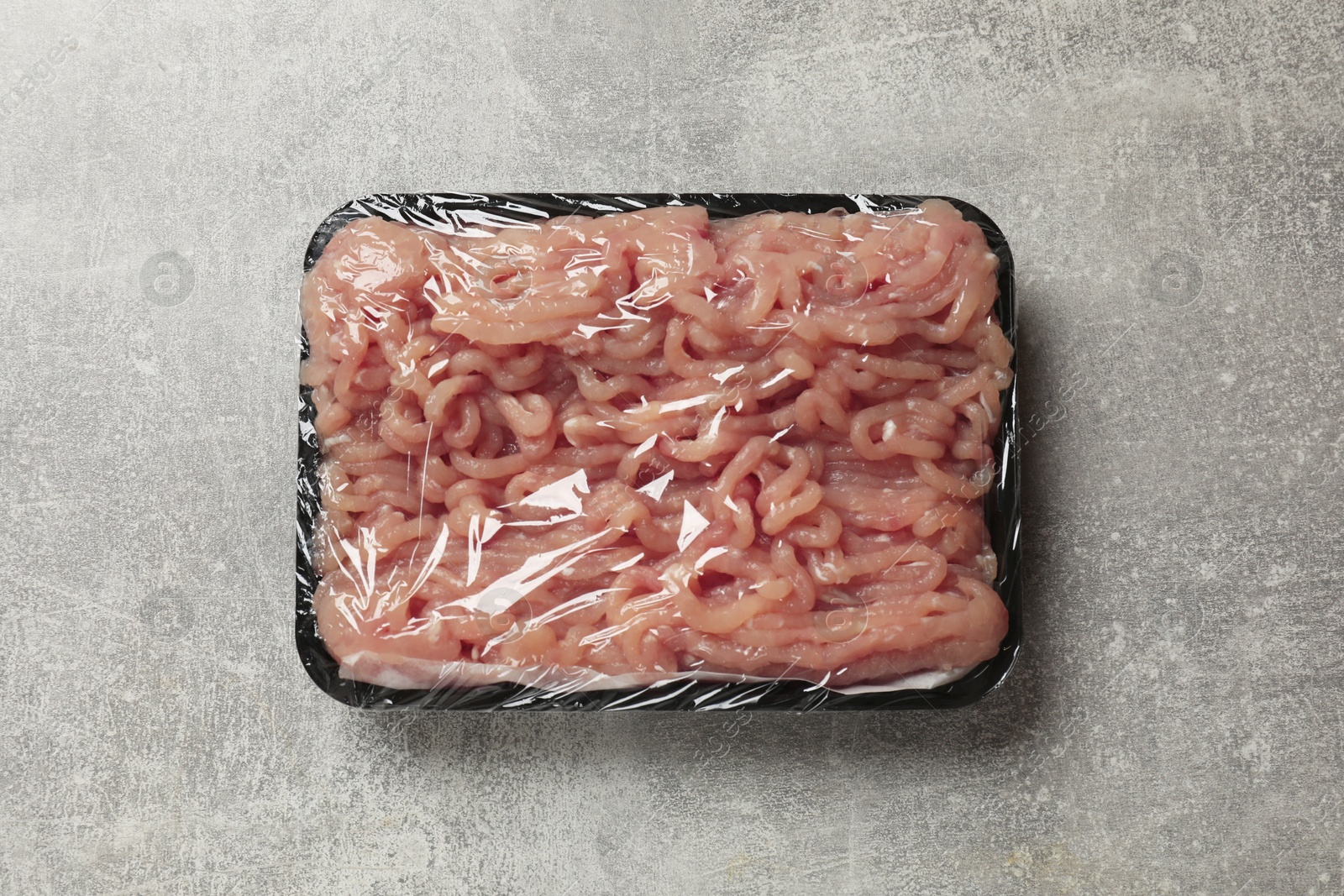 Photo of Plastic pack with fresh minced meat on grey textured table, top view