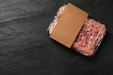 Photo of Plastic pack with fresh minced meat on black textured table, top view