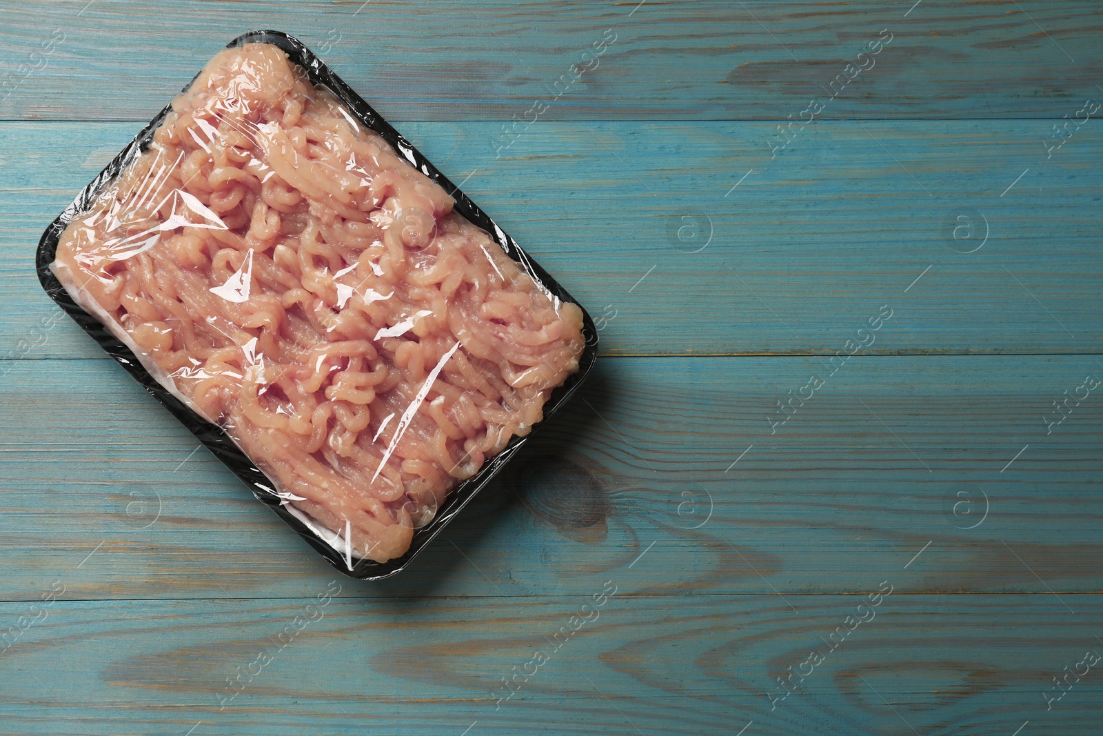 Photo of Plastic pack with fresh minced meat on blue wooden table, top view. Space for text