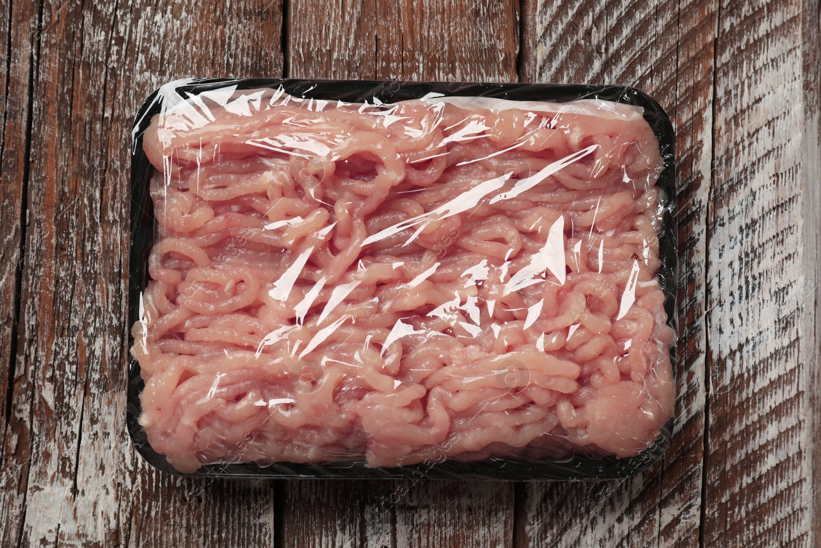 Photo of Plastic pack with fresh minced meat on rustic wooden table, top view