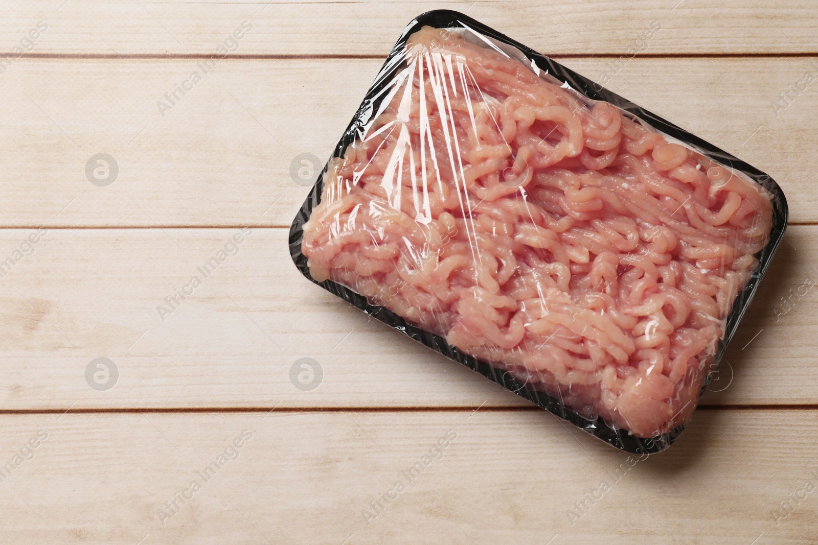 Photo of Plastic pack with fresh minced meat on light wooden table, top view. Space for text