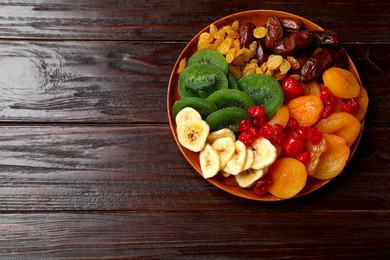 Photo of Mix of different dried fruits in bowl on wooden table, top view. Space for text