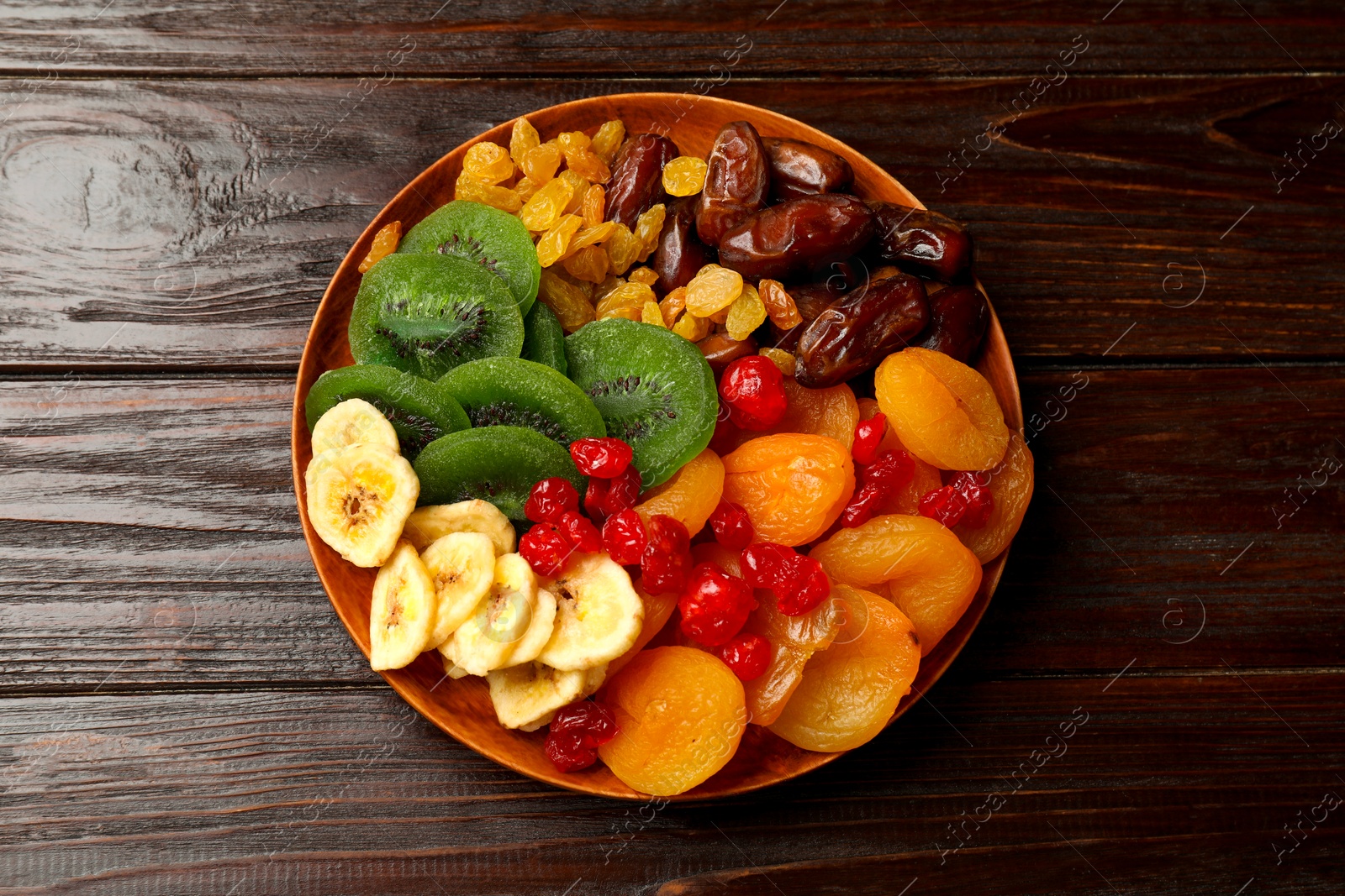 Photo of Mix of different dried fruits in bowl on wooden table, top view