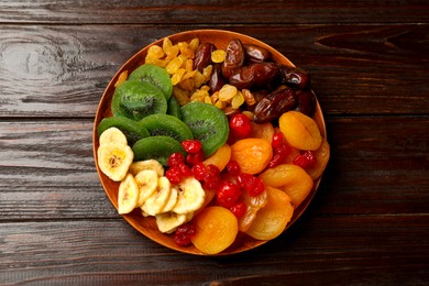 Photo of Mix of different dried fruits in bowl on wooden table, top view